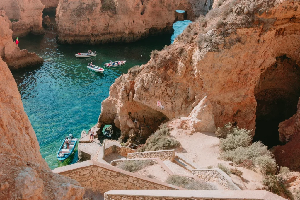 Small boats in a turquoise inlet beneath warm limestone cliffs at Ponta da Piedade in Lagos