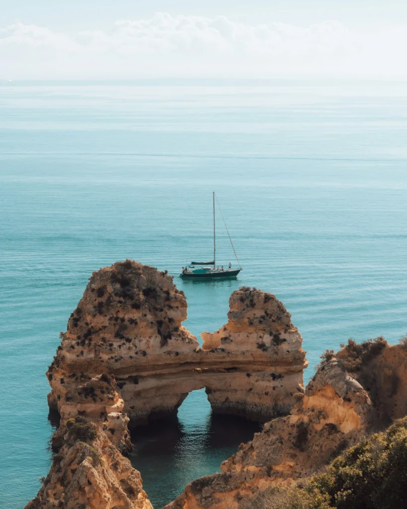 Sailing boat beyond a rock arch on the coast at Praia do Camilo in Lagos