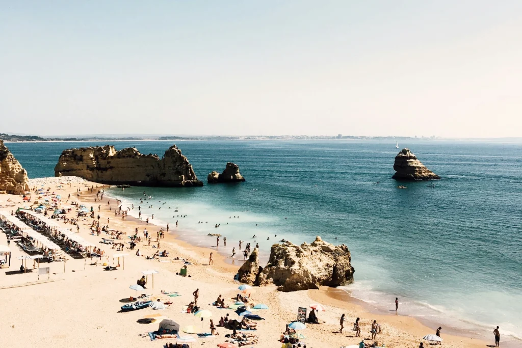 Sunlit sand, beachgoers and offshore rock formations at Praia de Dona Ana in Lagos